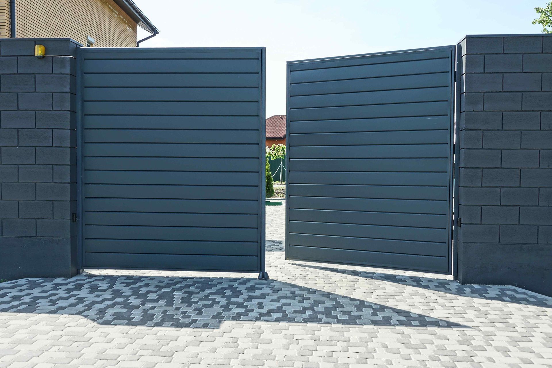 A black gate is open to a driveway next to a brick wall.