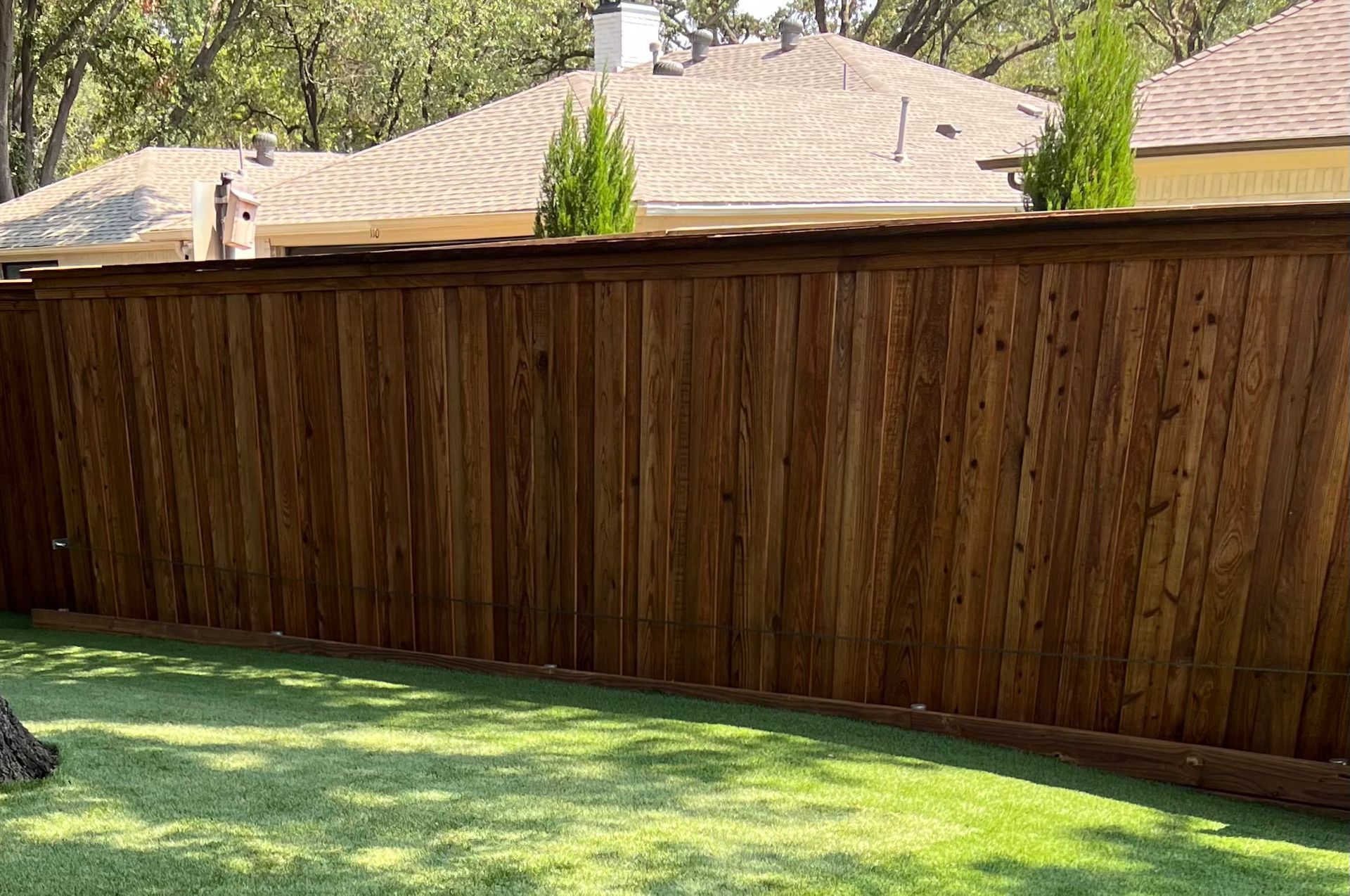 A wooden fence surrounds a lush green lawn in a backyard.