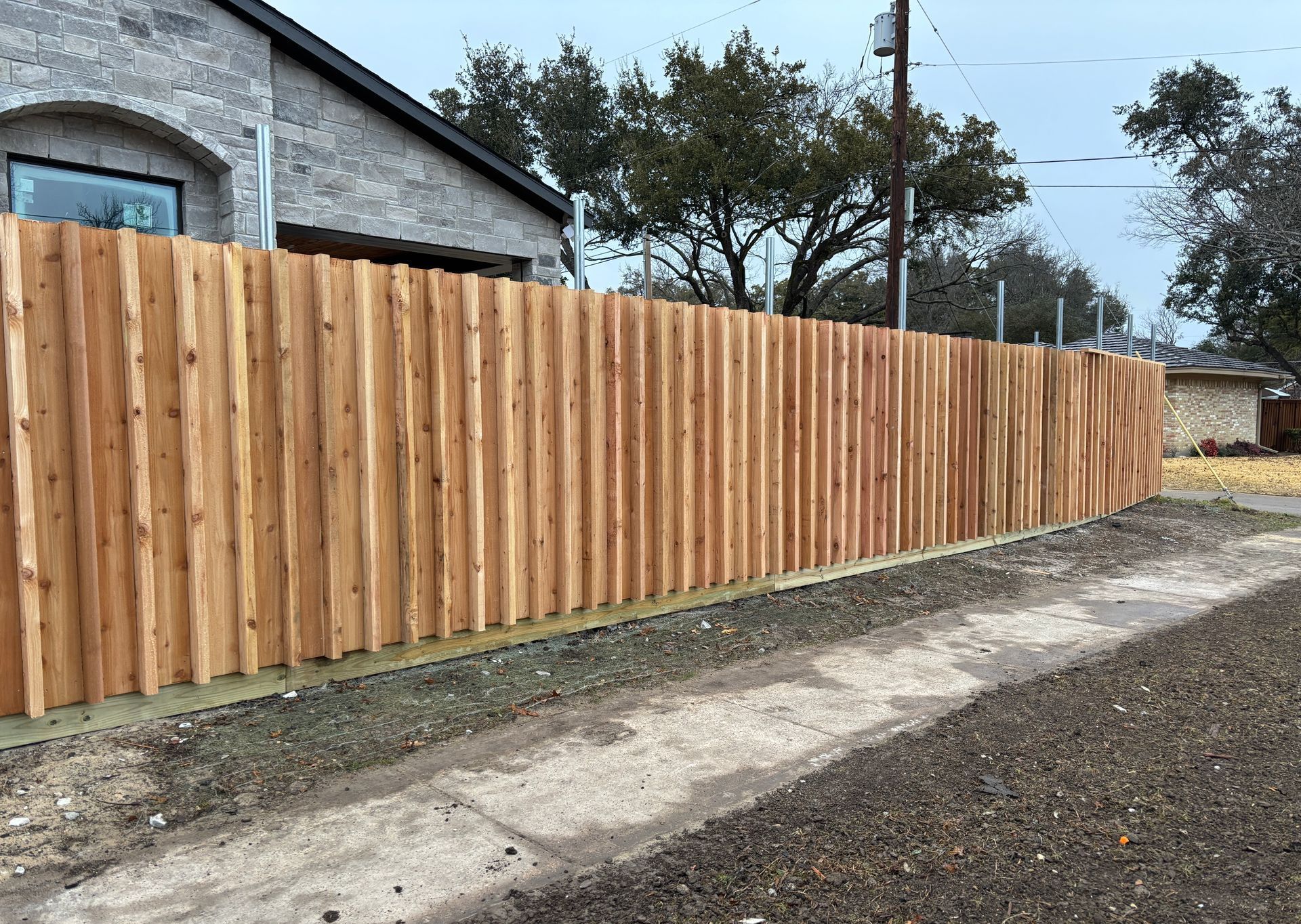 A wooden fence is sitting on the side of the road next to a house.