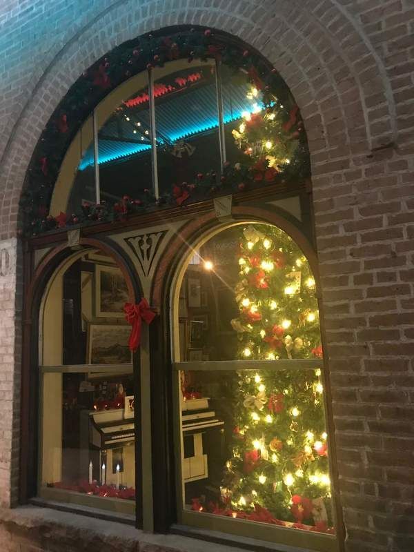Christmas window display with tree, garlands, and model house, reflected in arched window.