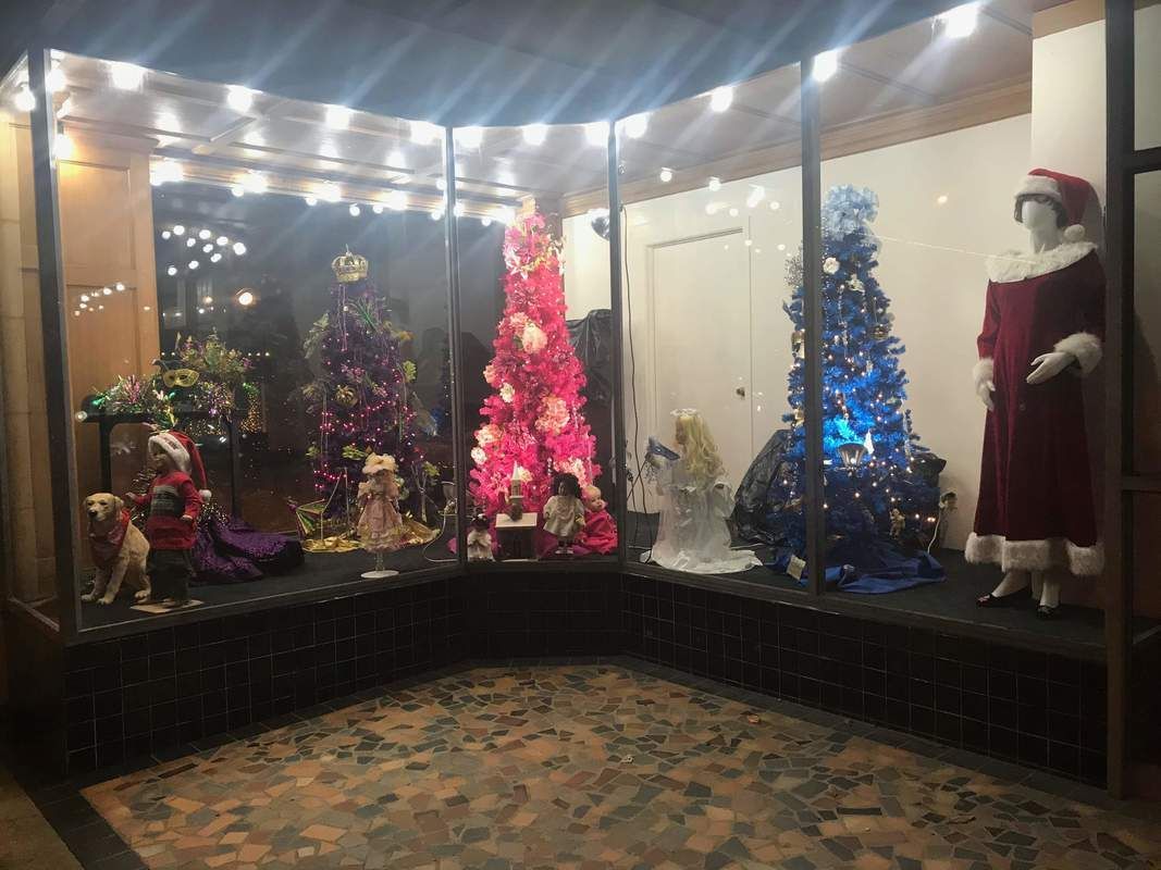 Holiday window display featuring colorful Christmas trees and a Santa costume.