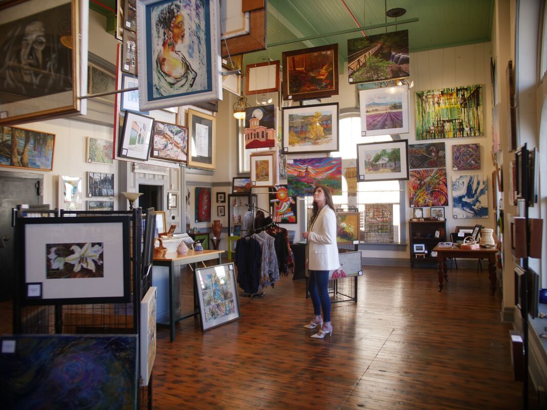 Art gallery interior with paintings on walls and hanging from the ceiling; a person stands near the center.