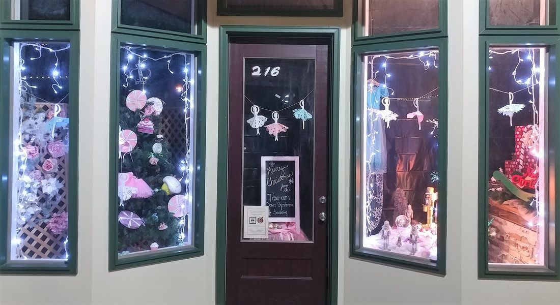 Storefront with decorated windows and a dark brown door. Pink flowers and lights are visible.