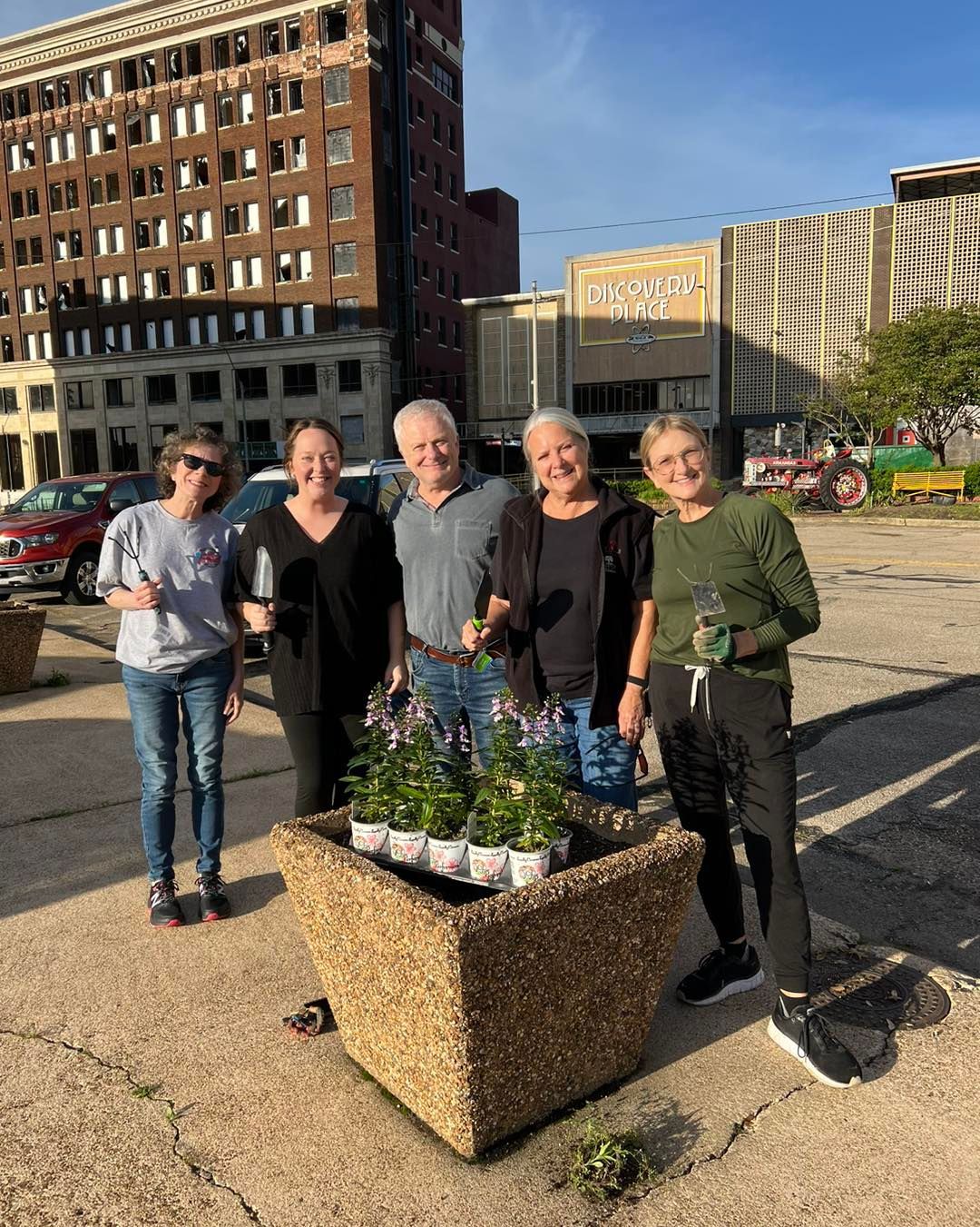 Five people pose with a planter filled with flowers in front of a building.