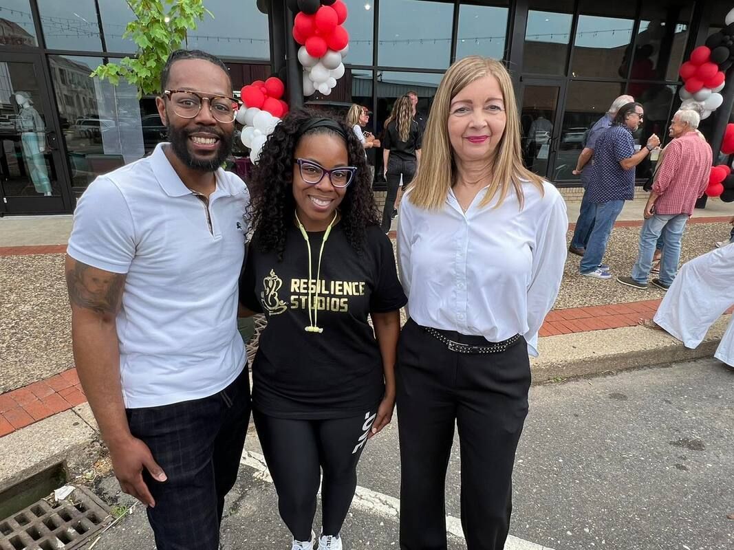 Three people smiling in front of a building with red and white balloons.