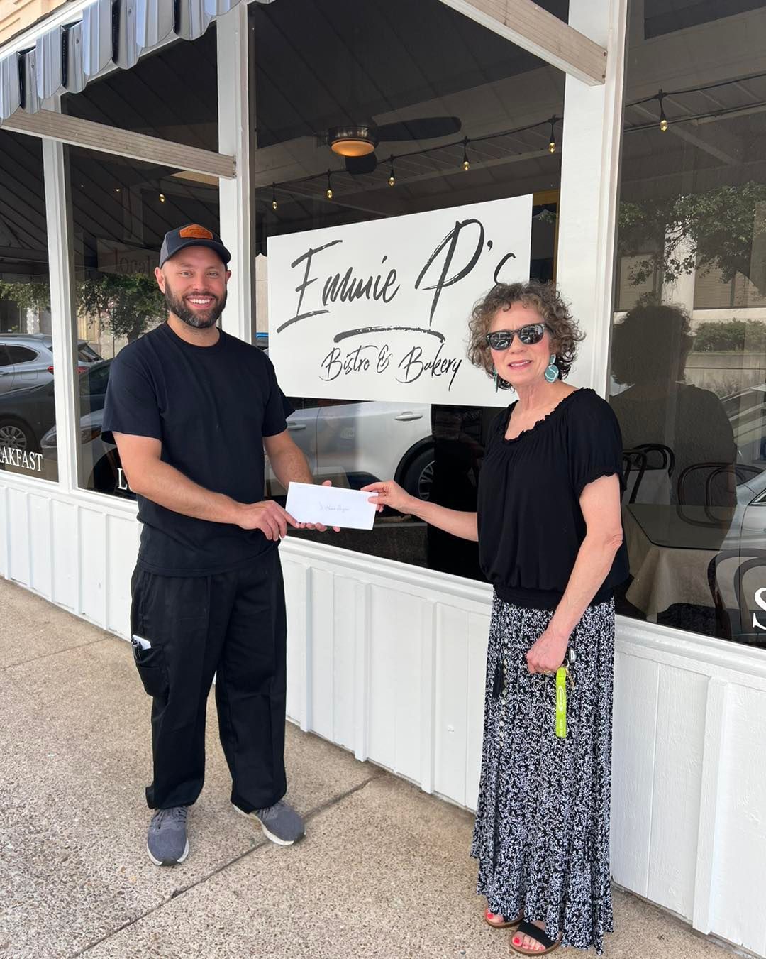 Man in black shirt receives a check from a woman outside 