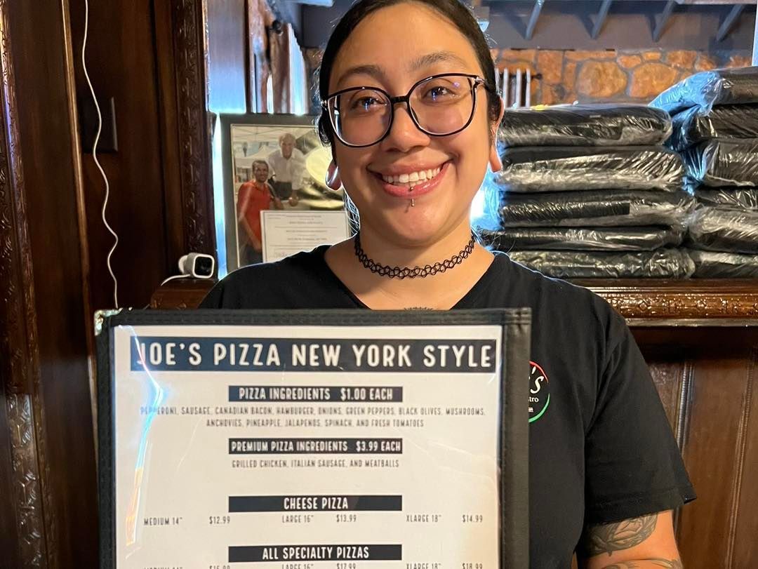 Woman holding Joe's Pizza menu, smiling inside a restaurant.