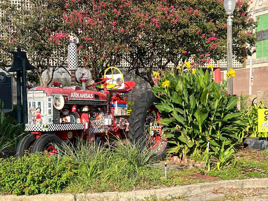 Decorated red tractor with black tires in a garden, with yellow flowers and a checkerboard pattern.