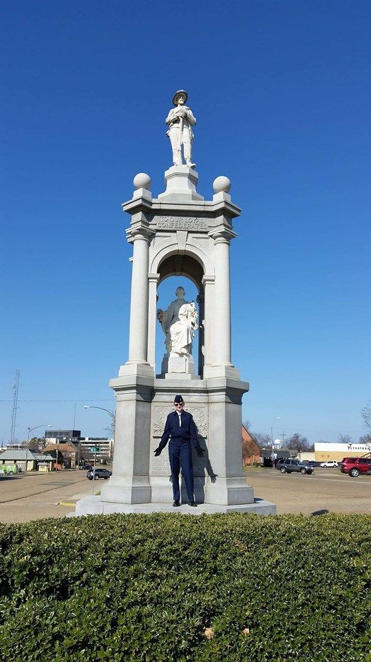 Statue with person, blue suit, standing in front; sunny day, clear blue sky.