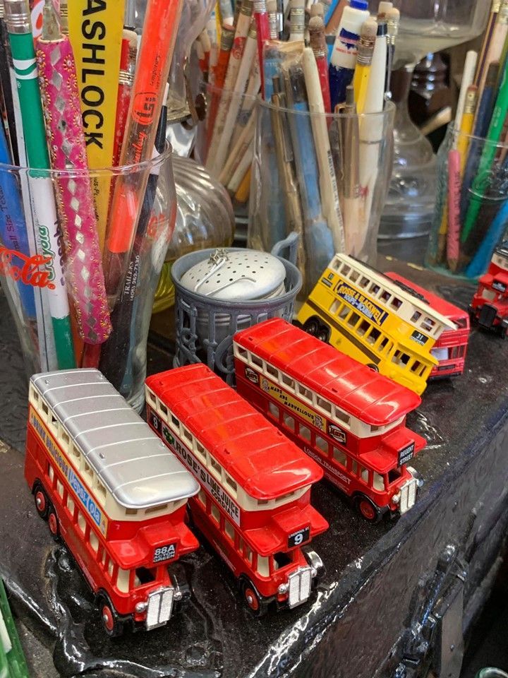 Toy double-decker buses in red and yellow near pencils in glass containers.