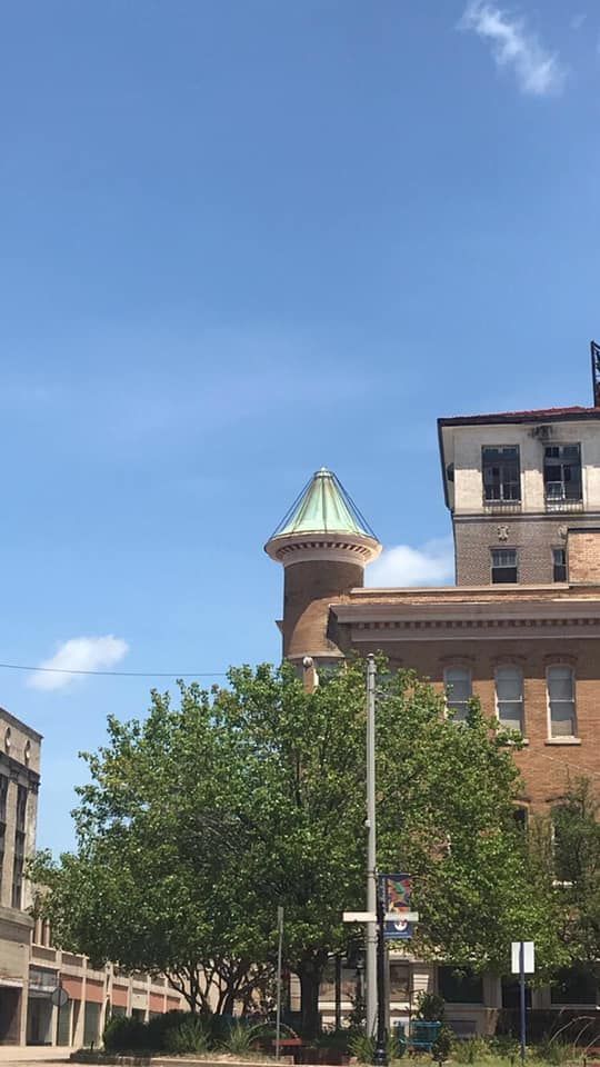 Buildings and a tree against a blue sky, with a tower featuring a green roof.