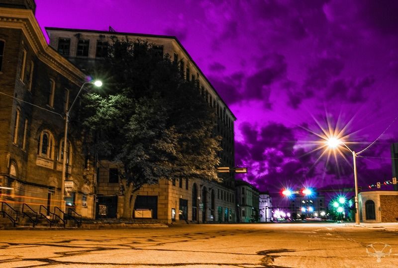 Street scene at night with purple sky. Buildings and street lights illuminated.