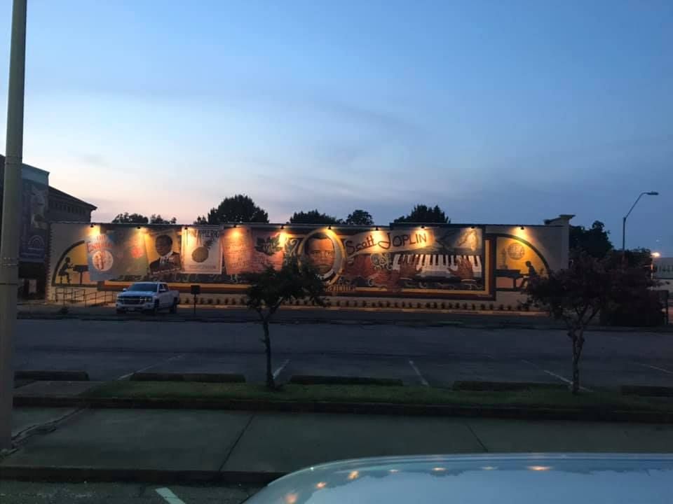 Mural depicting musicians and instruments, illuminated against a dusk sky.