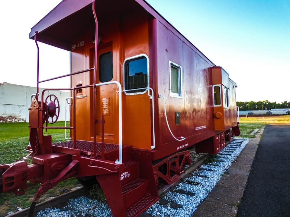 Red caboose on tracks, with steps and a viewing cupola, outdoors on a sunny day.