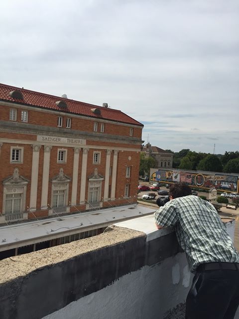 Person looking over a ledge at a large brick building with white columns and a red-tile roof.