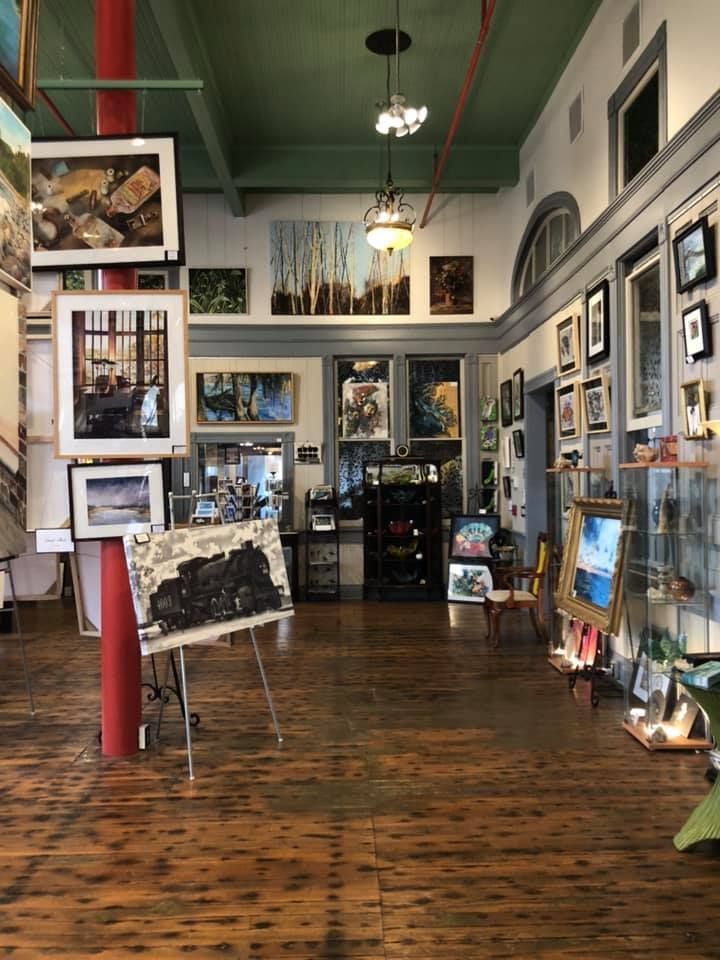 Art gallery interior with paintings on walls and display stands, hardwood floor, red pillar.
