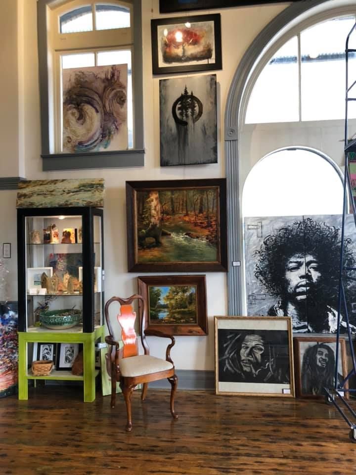 Gallery with art on display: paintings, portraits, and a glass cabinet on a wooden floor.