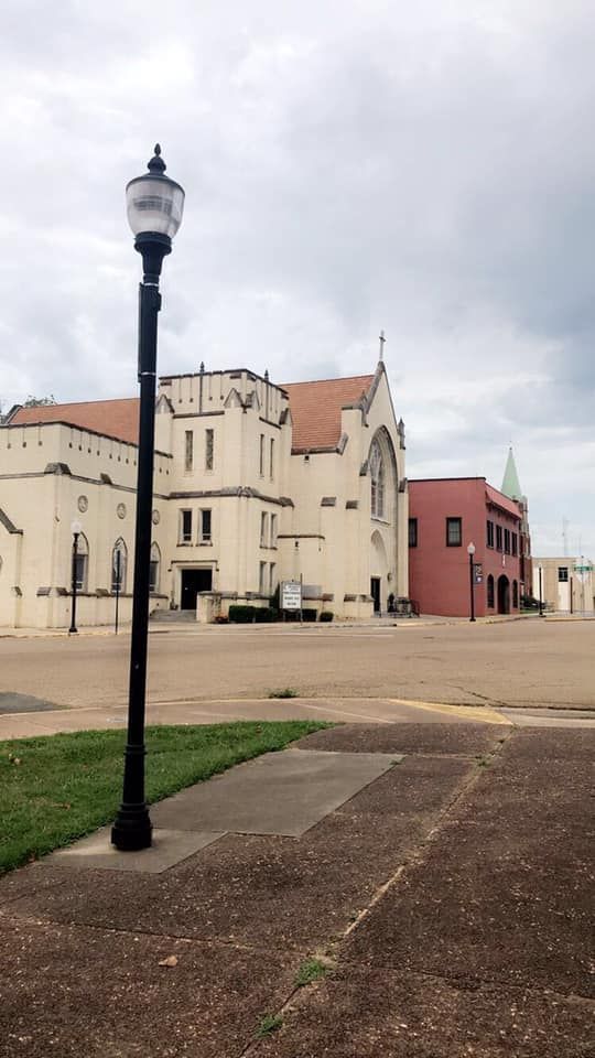 A tall black lamppost stands in front of a large white church on a cloudy day.