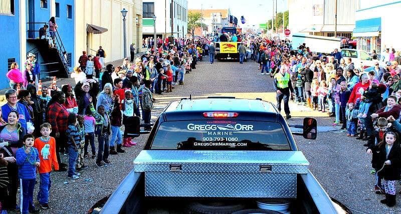 Parade with crowds lining the street; a truck with a toolbox in the bed leads the way.