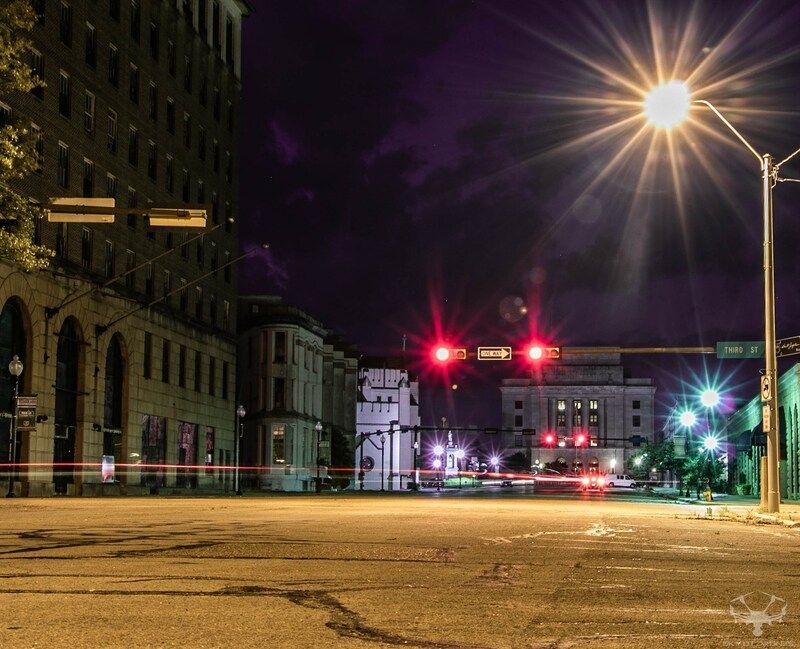 Nighttime city street scene with buildings, streetlights, and traffic signals; light streaks from passing vehicles.