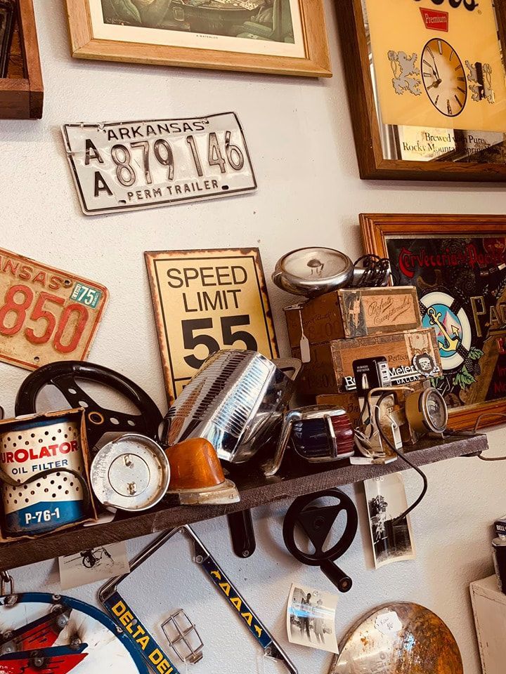 Shelf of vintage items, including license plates, a speed limit sign, car parts, and framed art.