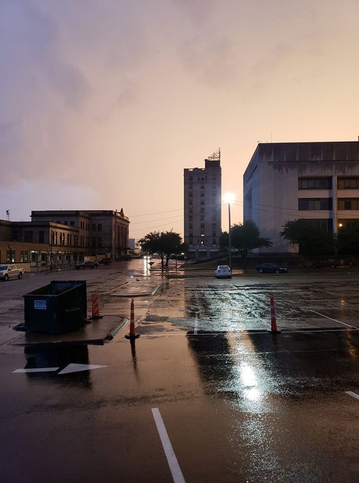 Wet city street with reflections under a cloudy, twilight sky. Buildings and streetlights.