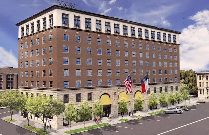Hotel building with brick facade, American and Texas flags, and arched entrance.