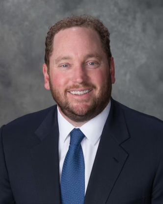 Man in suit and tie smiling at the camera against a gray background.