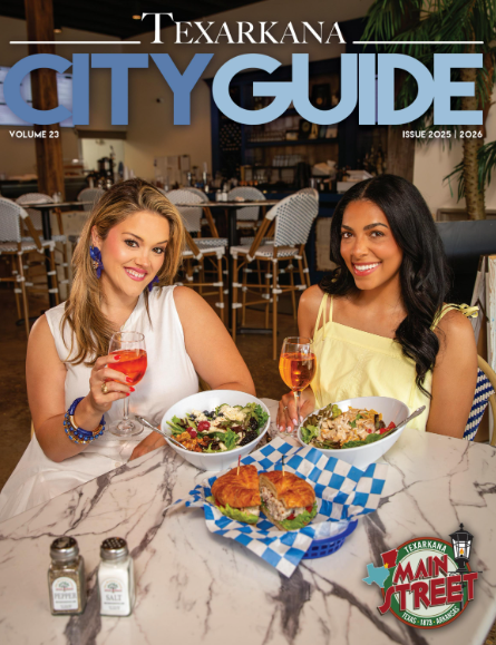 Texarkana City Guide cover: Two women smile, dine at a restaurant, holding drinks and food on a marble table.