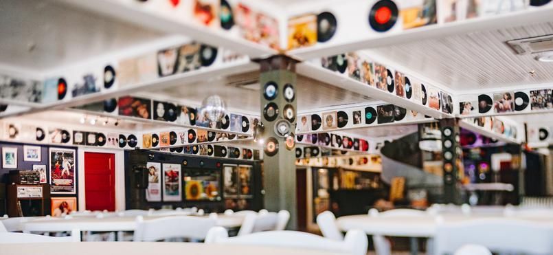 Interior of a cafe decorated with vinyl records and album covers. White tables, exposed beams, and red accents.