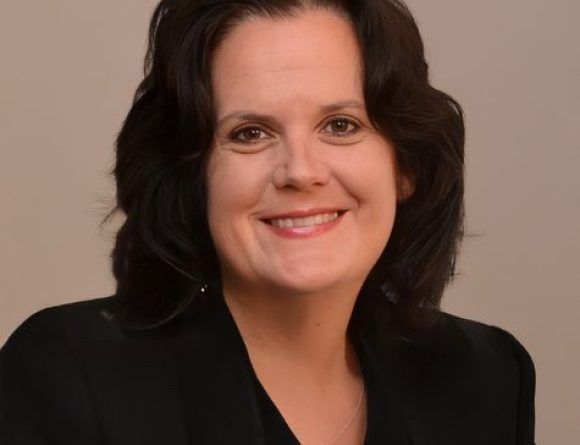 Woman with dark hair smiles, wearing a black blazer.