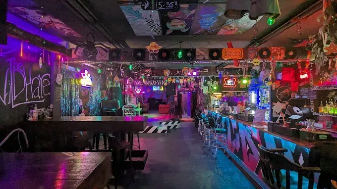 Interior of a neon-lit bar with graffiti, vinyl records, and decorations.