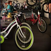Bicycles for sale inside a shop. A woman is in the background. Several bicycles are on display, some with white tires and colored rims.