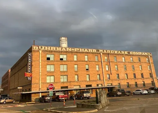 Brick building: Buhrman-Pharr Hardware Company, tall water tower, parked cars, cloudy sky.