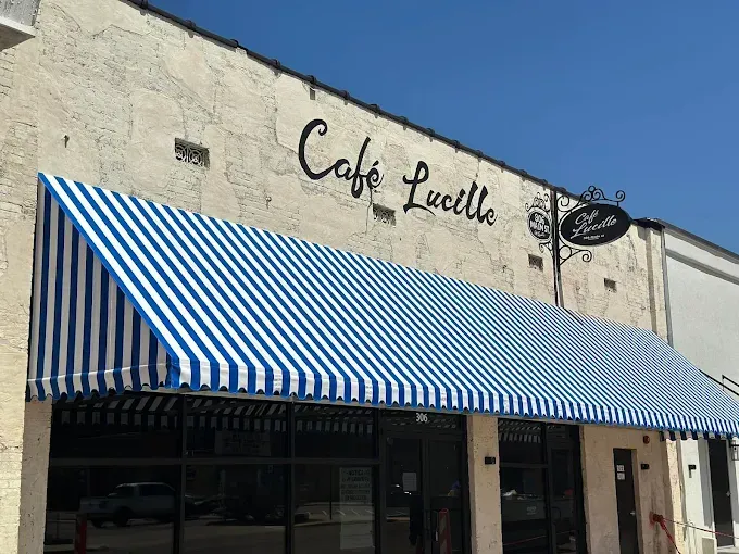 Cafe Lucille storefront with blue and white striped awning and black sign.