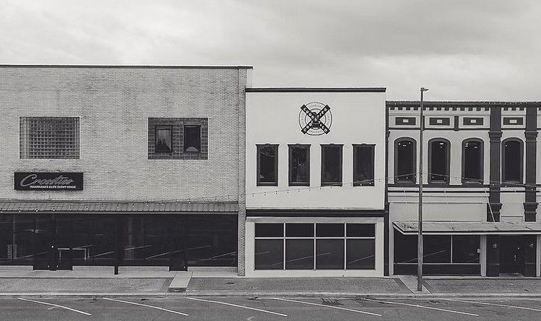 Buildings on a street, with varying architectural styles. A cloudy sky is overhead.