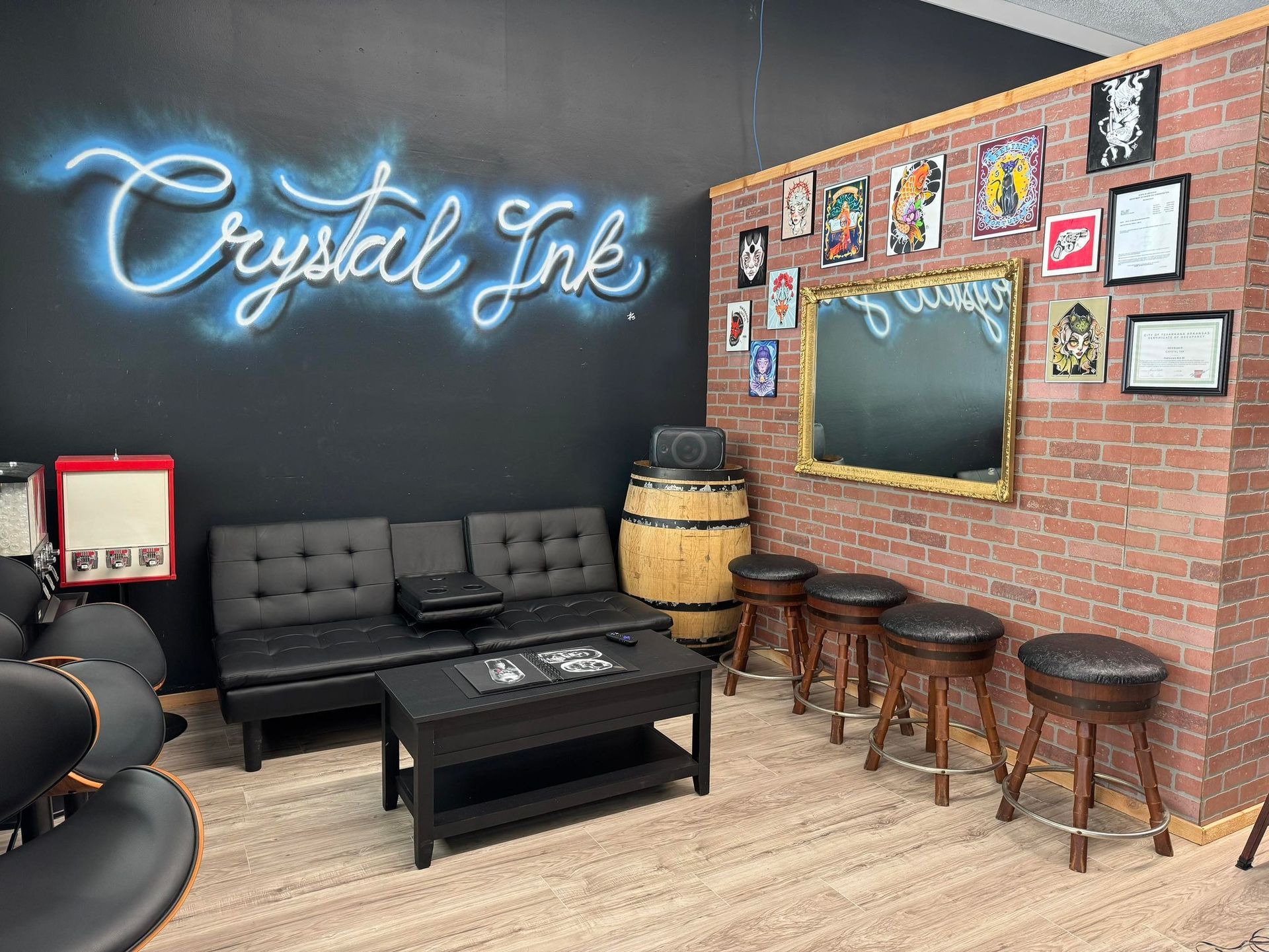 Interior of Crystal Ink tattoo studio, with neon sign, brick accent wall, couch, stools, and barrel.