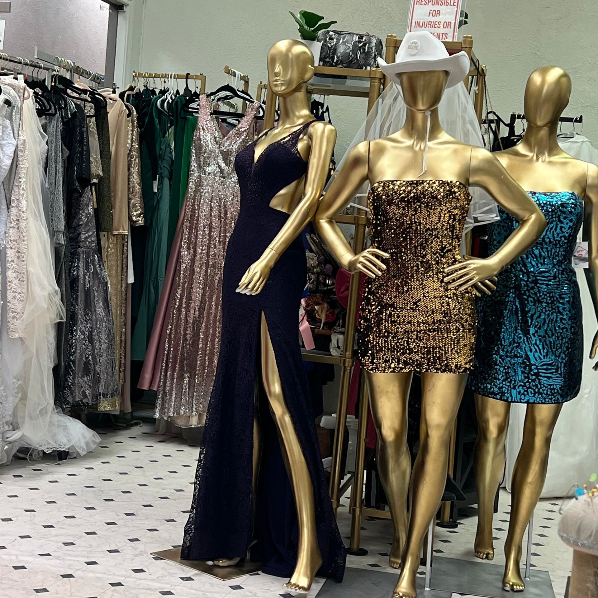 Clothing store interior. Gold mannequins display gowns and dresses in front of clothing racks with various dresses.