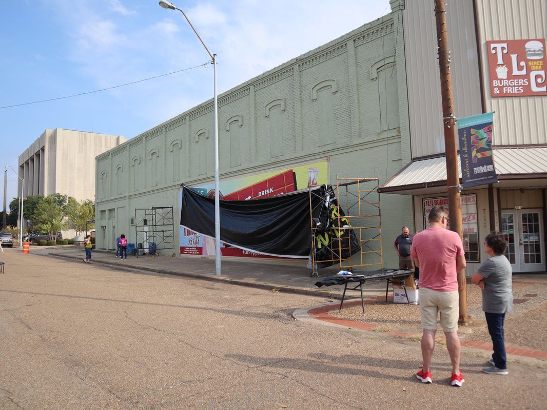 Street view of a light green building with a black sheet covering something. People stand nearby.