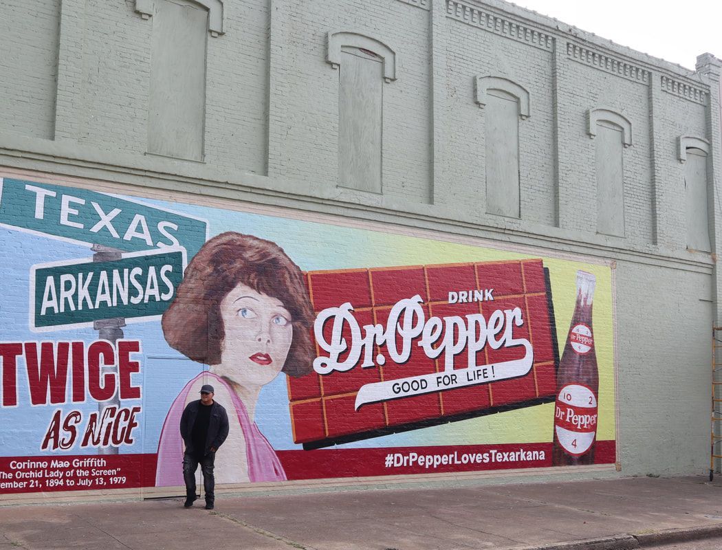 Man stands before a Dr. Pepper mural on a brick wall, with a state sign and text 
