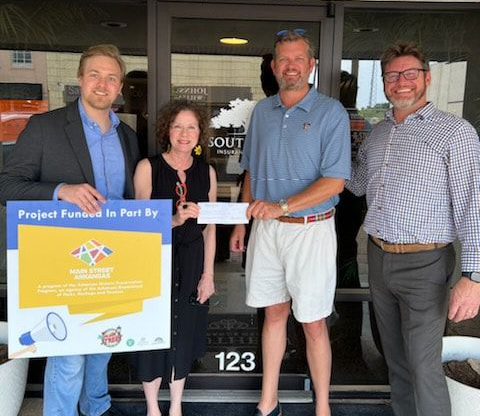 Four people holding a sign and a check outside a building with the number 123.