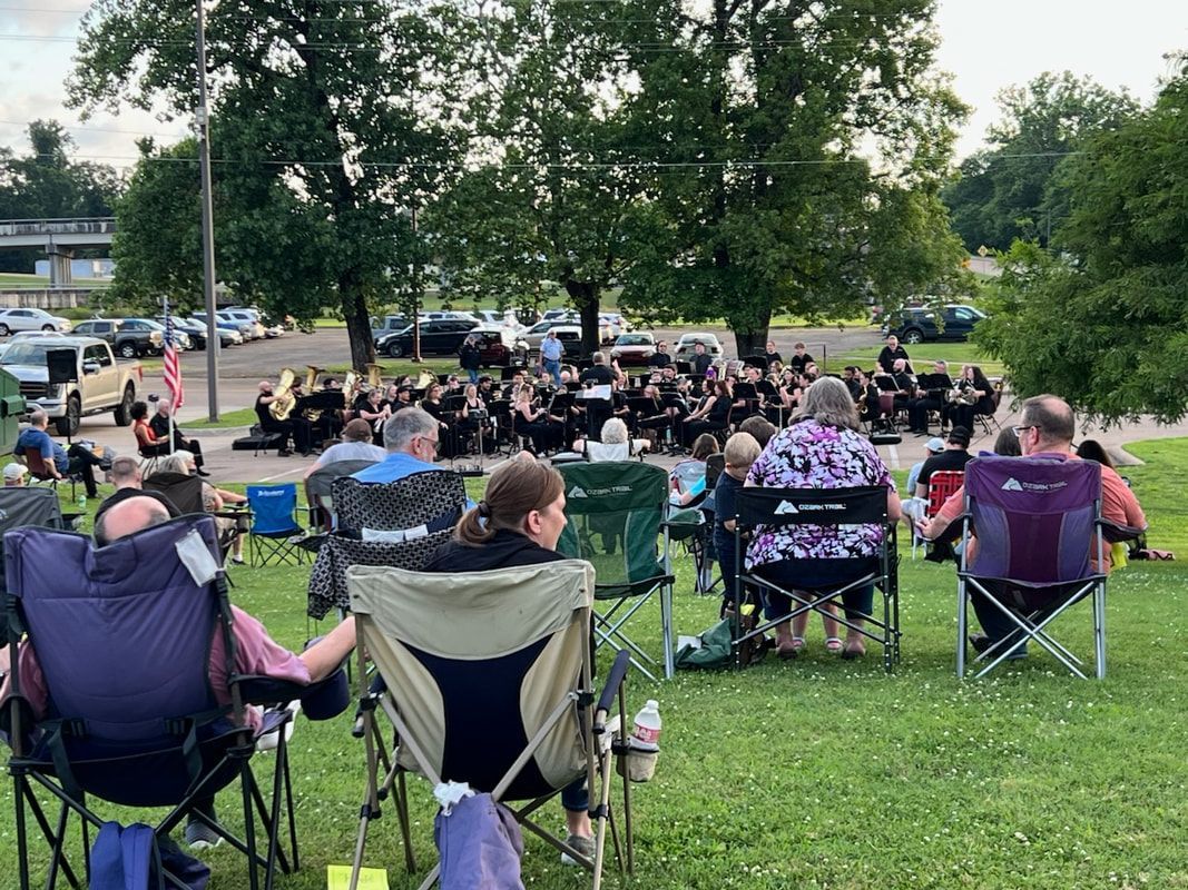 People seated in folding chairs watching a band perform outdoors on a grassy area.