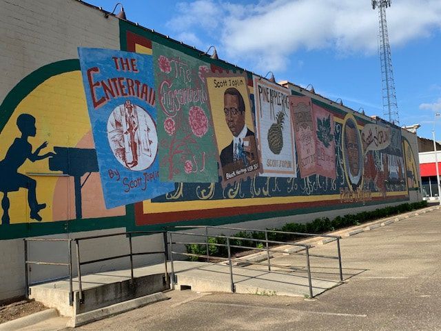 Mural on a building, depicting entertainment posters and a person playing piano; outdoors with a cloudy sky.