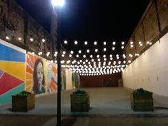 An open-air area at night with string lights, planters, and murals on the walls.