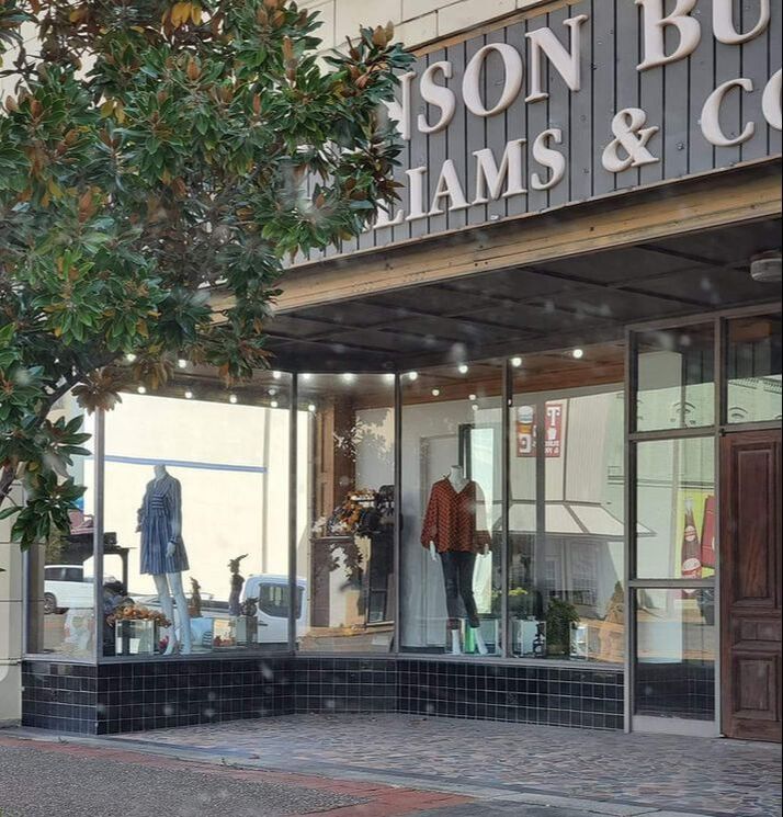 Clothing store window display with mannequins. Sign reads