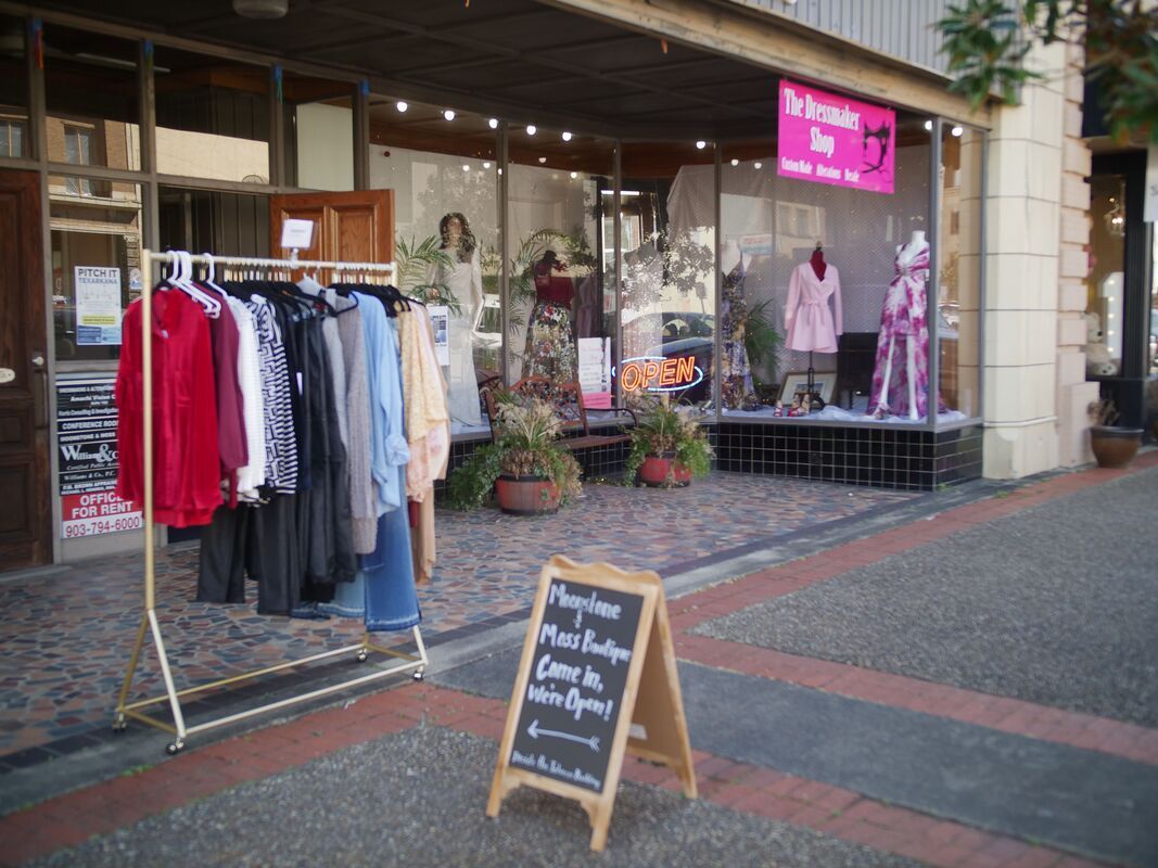 Clothing boutique storefront with clothes rack outside; sign advertises discounts.