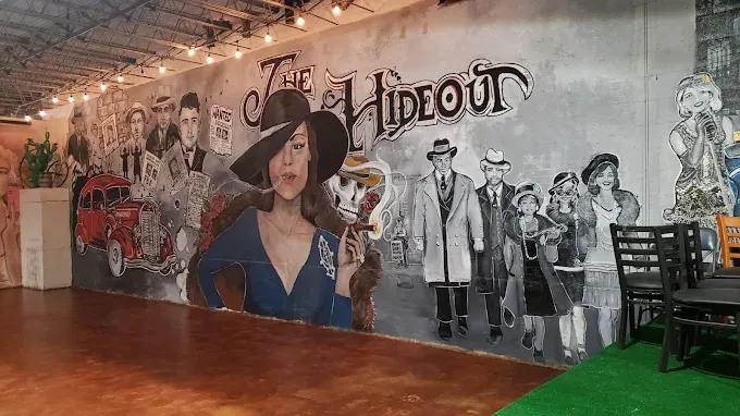 Mural inside The Hideout featuring vintage imagery: woman with a hat smoking a cigar, alongside other figures and a red car.