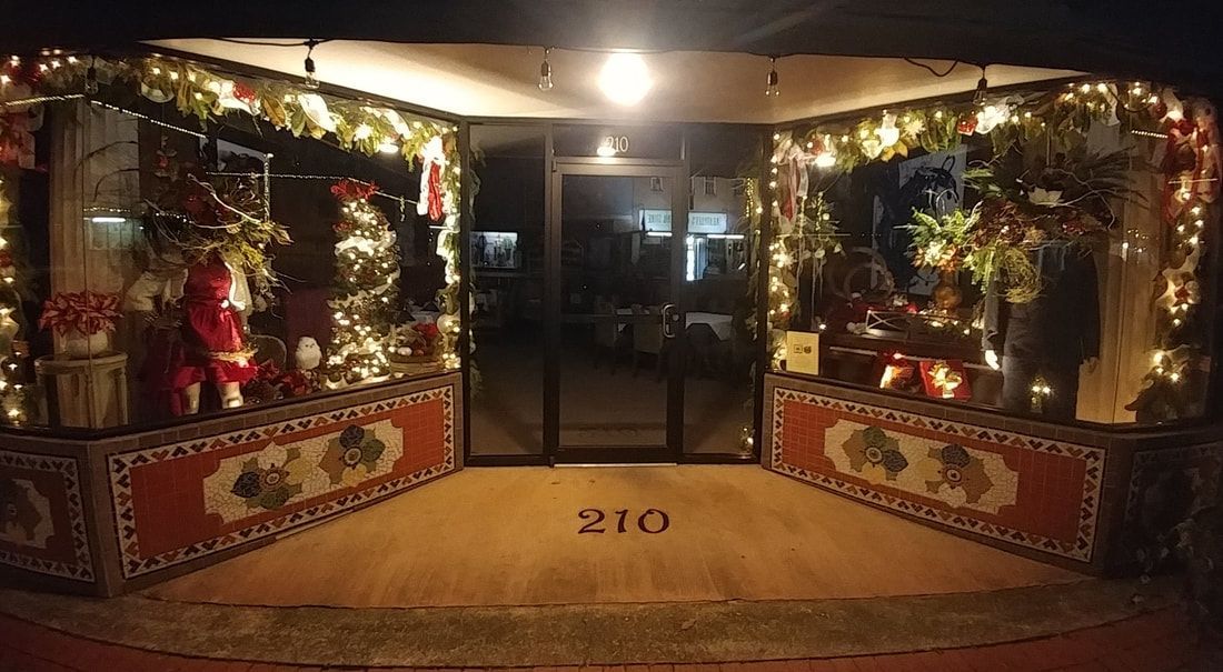 Storefront decorated for Christmas, garlands of lights, Santa figure visible, address 210.