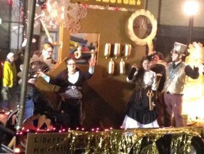 Steampunk-themed parade float with costumed figures waving. Gold and brown accents, outdoor setting.