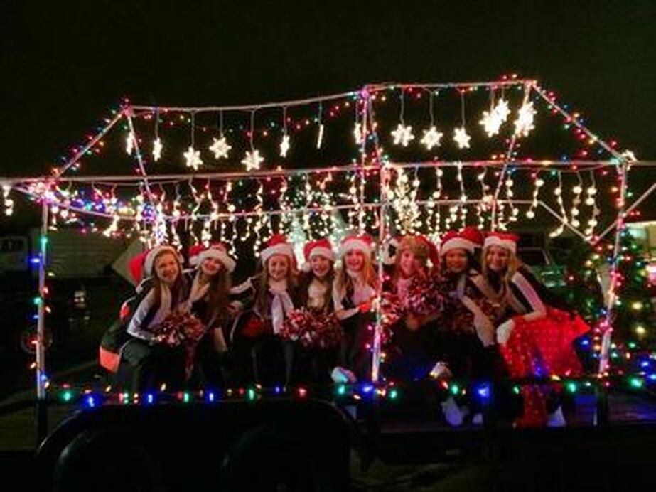 A group of people wearing Santa hats on a trailer decorated with Christmas lights at night.